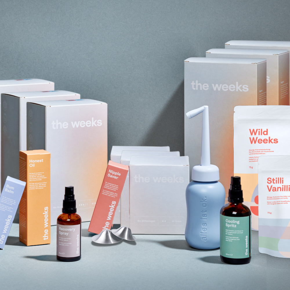 Everything Wochenbett-Box von the weeks. Es sind Schachteln von großen Wochenbetteinlagen, kleinen Wochenbettbinden, Stilleinlagen, Nippel Saver, Honest Oil zu sehen. Das Recovery Spray steht in der Flasche dort, genauso wie die Podusche. Zusätzlich Cooling Spritz, Bum Balm, Wochenbett-Tees Stilli Vanilli und Wild Weeks und Silberhütchen.