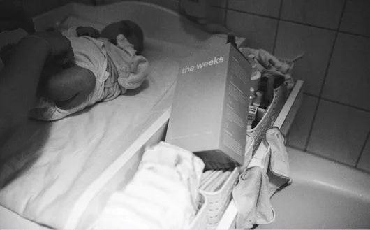 Baby wird auf Wickeltisch über der Badewanne gewickelt, daneben liegt eine Packung der Wochenbettbinden von the weeks