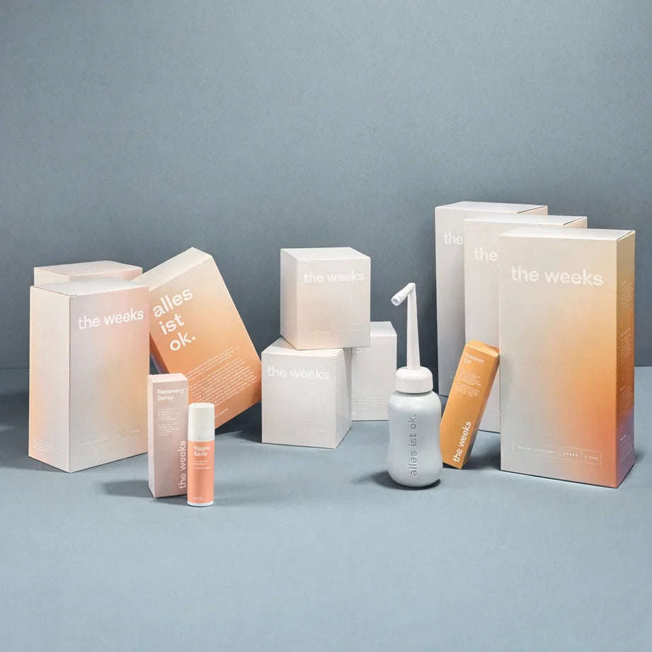 WHOLE Wochenbett-Box von the weeks. Es sind Schachteln von großen Wochenbetteinlagen, kleinen Wochenbettbinden, Stilleinlagen, Nippel Saver, Honest Oil zu sehen. Das Recovery Spray steht in der Flasche dort, genauso wie die Podusche.