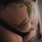 Bauch einer Schwangeren frontal mit Tattoos, das Honest Oil von the weeks läuft auf dem Bauch herunter