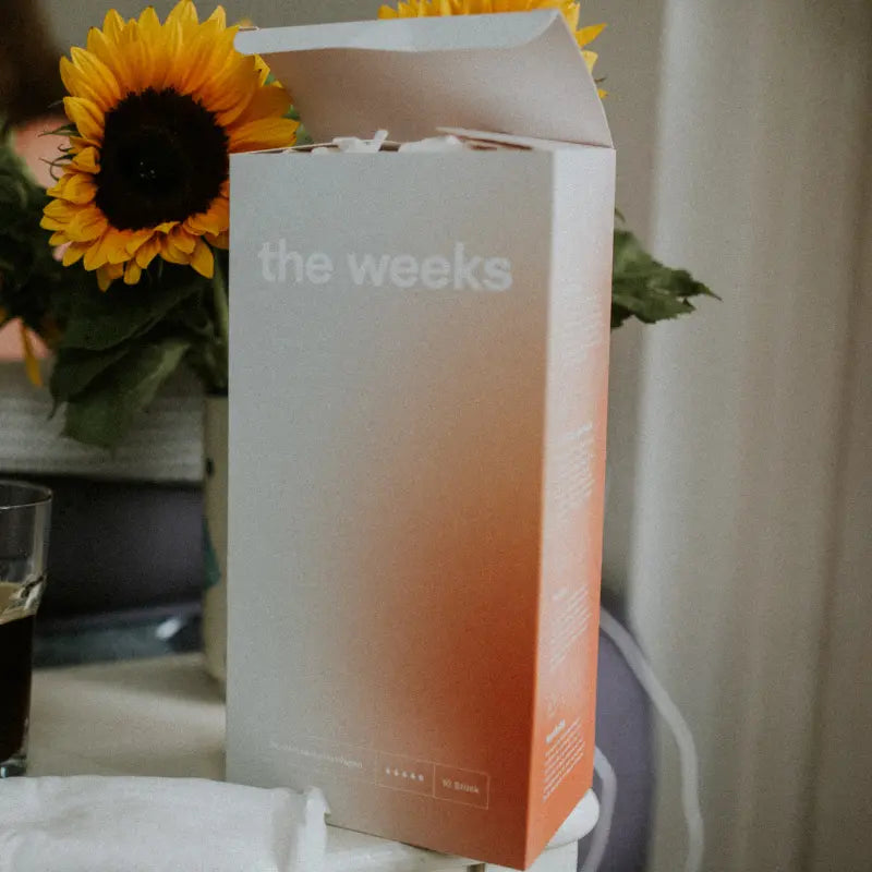 Bio-Wochenbetteinlagen von the weeks stehen zusammen mit einem Strauß Sonnenblumen auf einem Nachttisch