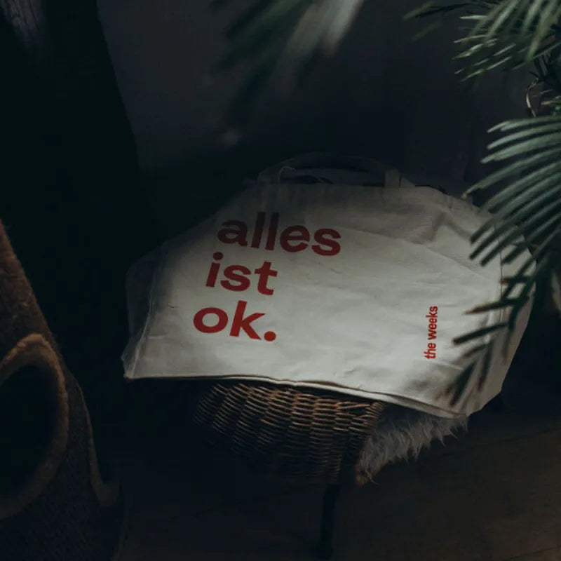 Wekkender-Bag "alles ist ok." von the weeks liegt auf einem Basthocker