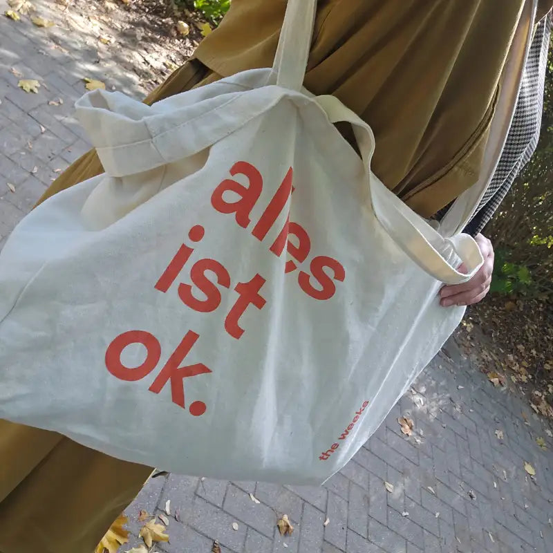 "alles ist ok."-Tasche von the weeks auf einem Spielplatz über die Schulter einer Frau gehängt